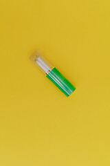 Lipstick with a bright green cap on a yellow background