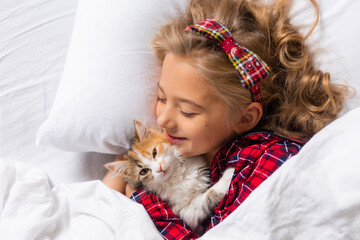 a cute little girl is sleeping sweetly at home in a rabbit with a kitten. White cotton bed linen. Christmas holidays. Children and pets at home