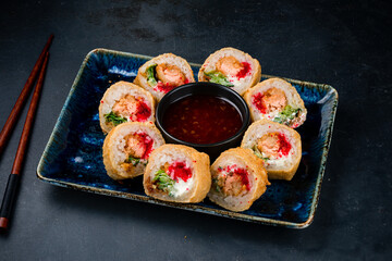 Set of tempura sushi rolls with salmon in batter, cream cheese, cucumber, lettuce, flying fish caviar and sauce.