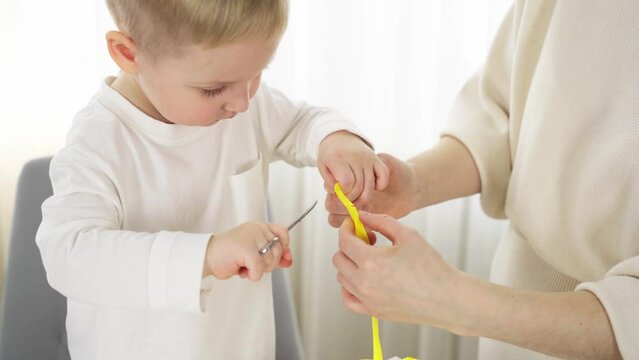 A little boy cuts a yellow gift wrapping ribbon with scissors. Mom is standing next to me. Close-up.