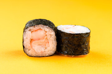 Mini sushi rolls with shrimp, rice and nori on yellow background.