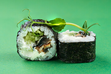 Mini sushi rolls with smoked eel, cucumber and cream cheese on green background.