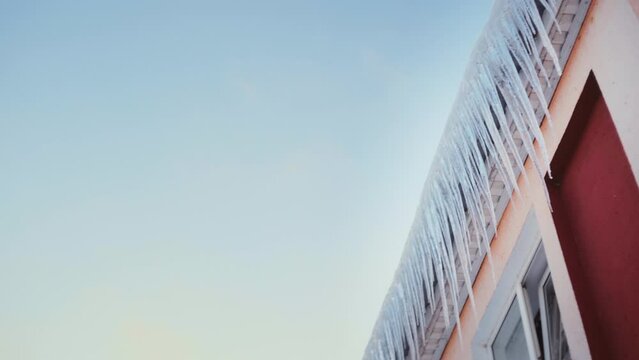 Large icicles hang from the overhang of the roof of the building. Falling ice- winter hazard for passersby