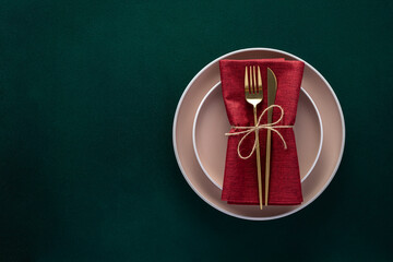 Dinner table setting with empty plates and golden cutlery on dark green background, card or menu...