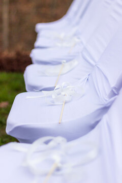 Sticks with ribbon and bell attached lay on chairs with white covers.