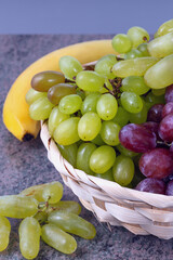 berries of white and red grapes and fresh fruits in a straw basket on a dark wooden background