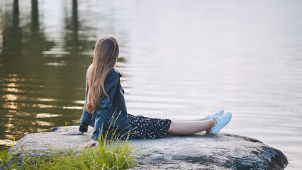 A girl sits by the lake on a rock.