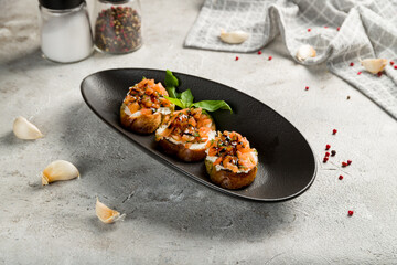 bruschetta with tomatoes and cheese on black plate on grey table