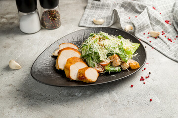 Salad caesar with chicken on black plate on grey plate