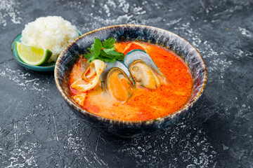 Tom Yam soup with mussels and shrimps on grey table
