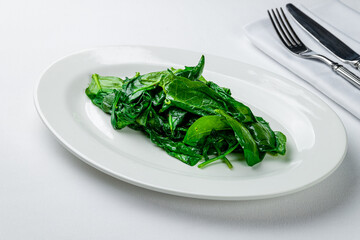 Garnish steamed spinach on a white plate on white table