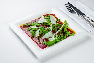 Beef carpaccio with Parmesan and arugula on white plate