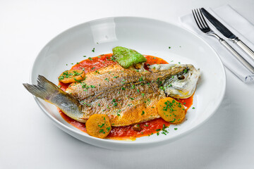 Fried sea bass with tomato sauce, potatoes and spices on white plate