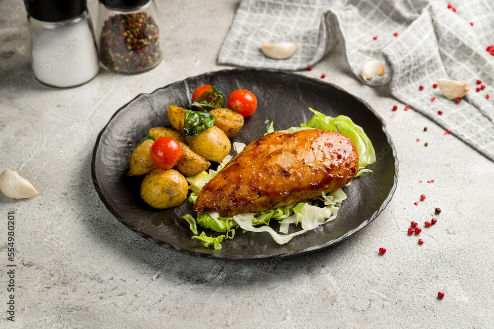 Wall mural Grilled chicken Breasts with mini potatoes and tomatoes on black plate on grey table