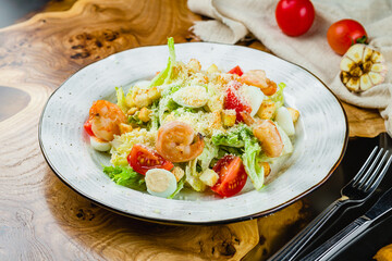 salad caesar with shrimps on white plate on wooden table
