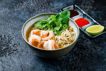 Vietnamese soup Pho with shrimps and noodles on dark stone table