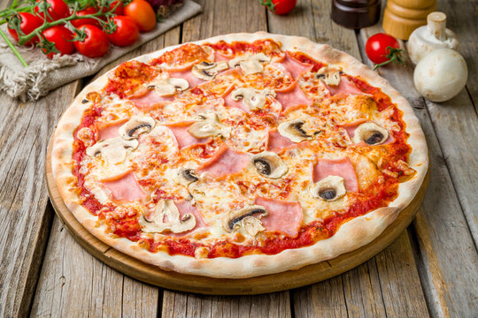 Pizza with ham and mushrooms with tomato sauce on wooden table, close up