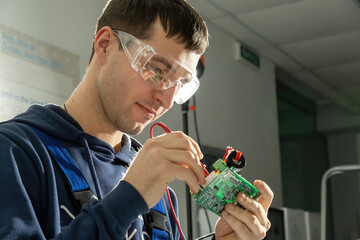 Technician works with motherboard soldering cables in equipped workshop. Foreman wearing special...