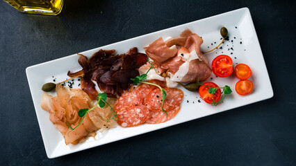 Set of sliced beef, chicken, pork ham, salami sausage, cherry tomatoes and microgreens.