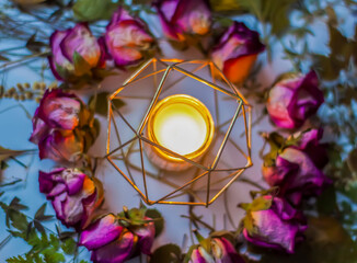 Dry rose flowers and burning candle in the metal candlestick. Decor for natural candles.