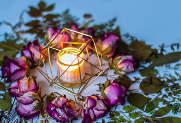 Fototapeta na wymiar Dry rose flowers and burning candle in the metal candlestick. Decor for natural candles.