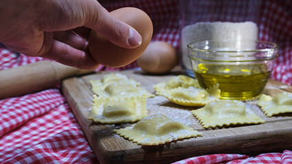 Persona sujetando un huevo para hacer pasta fresca en un fondo de cuadros rojos y blancos 