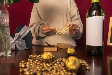 Persona sosteniendo un collar dorado sobre caja de regalo frente a mesa cubierta con chocolates en...