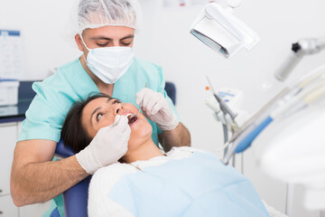 The dentist in face mask inspects female patient teeth with mirror and probe