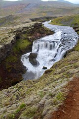 Naklejka na ściany i meble Majestic icelandic waterfall surrounded by green moss and grass with fresh glacier water. Icelandic weather. 