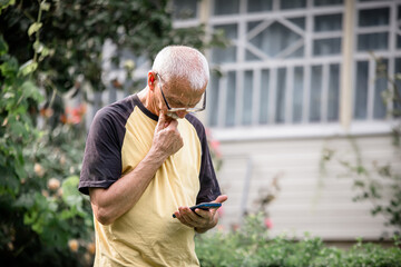 The old man holds his hand to his face and thoughtfully studies the instructions or listens to the...