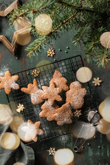 Christmas cookies or gingerbreads of various shapes on pastry cooling rack on green wooden table. Xmas or new year composition with fir tree and bokeh lights, top view