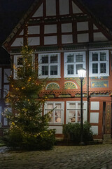 A Christmas tree with garlands stands near an ancient house at night