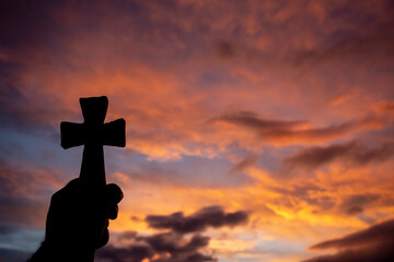 hand holds a cross in backlight at sunrise. selective focus. copy space