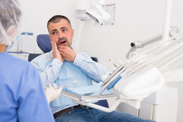 Female dentist talking to european male patient complaining of toothache at dental clinic office
