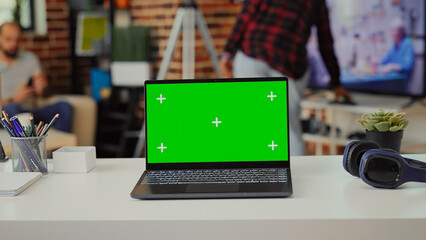 Laptop display showing isolated green screen on empty table at home, having blank chroma key template on wireless pc. Screen with copyspace mockup background in living room space.