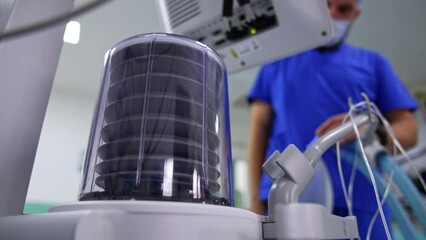Doctor looks at the pump of lung ventilator machine. Medic separates ambu bag from a tube and the pump falls and stops. Low angle view. Blurred backdrop.