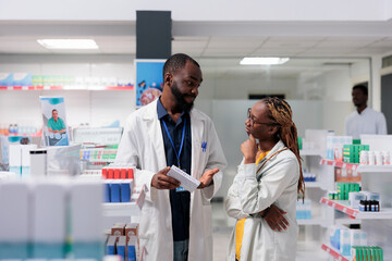 African american pharmacist consulting buyer in pharmaceutical drugstore, woman choosing...