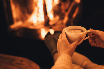 Woman drinkink hot cocoa sitting by the fire in front of cozy fireplace.