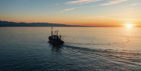 Fishing boat catching fish at sunset aerial view from drone. Small fishing trawler ship on sea surface.