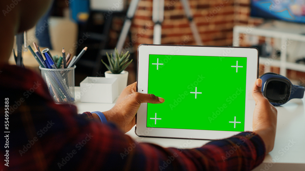 Poster female freelancer using horizontal greenscreen on wireless device, looking at blank chroma key templ