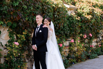 Beautiful bride girl in puffy wedding white dress and veil hugging handsome groom from the back....