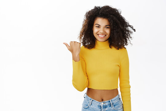 Smiling african american woman pointing finger left, showing advertisement, promo offer, standing against white background