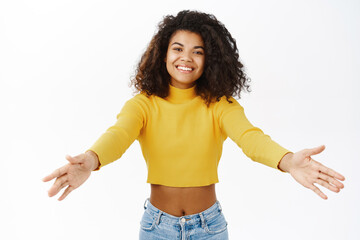 Smiling african woman reaching hands and hugging, cuddle, receive something, stretching arms, standing in stylish outfit over white background