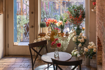 Multiple beautiful bouquets of various flowers are arranged in front of a window to create a romantic ambiance for a surprise proposal. 
