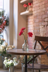 Beautiful red flowers in a vase are arranged to sit on a table creating a romantic ambiance for a surprise proposal. 