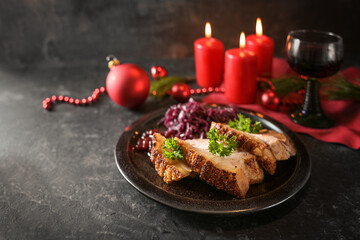 Fototapeta na wymiar Festive roast pork slices with red cabbage on a dark plate, red candles, wine and Christmas decoration against a dark background, copy space, selected focus
