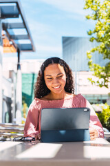 Latin university student woman smiling and using a tablet sitting outside the mall in her free time