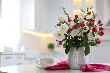 Vase with fresh flowers and cup on table in kitchen. Space for text