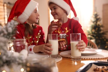 Cute little children with delicious Christmas cookies and milk at home, focus on hands