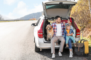 Parents, their daughter and dog sitting in car trunk near road, space for text. Family traveling...